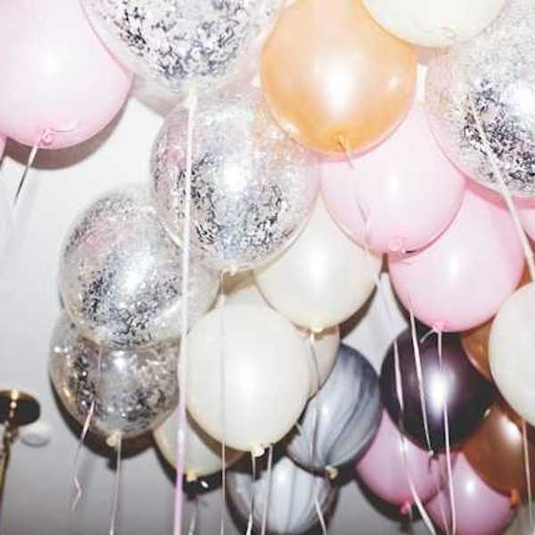A bunch of pink, white and silver balloons hovering against a ceiling