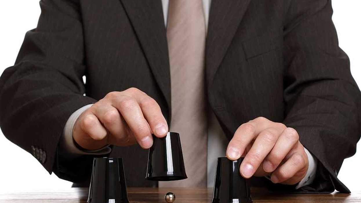 A business man playing a shell game with black plastic cups and a silver ball