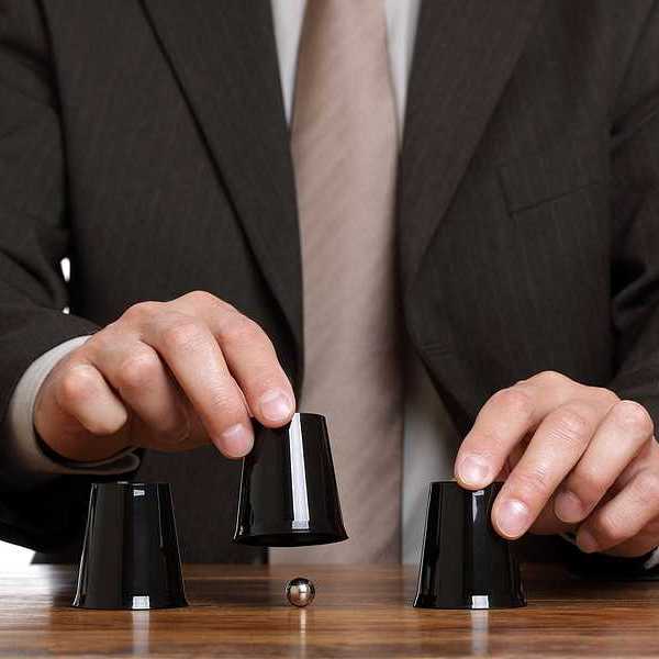 A business man playing a shell game with black plastic cups and a silver ball