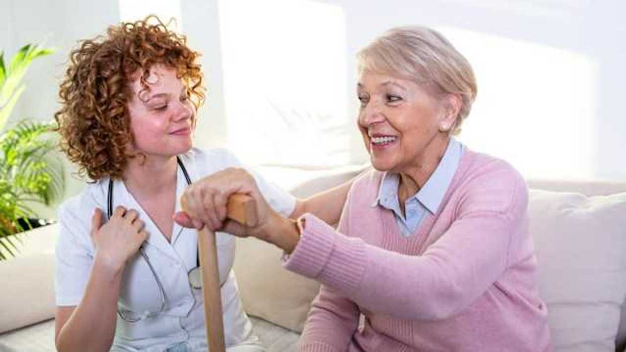 A caregiver and an elderly woman with a cane