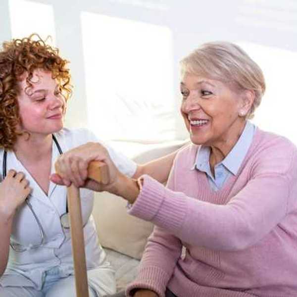 A caregiver and an elderly woman with a cane