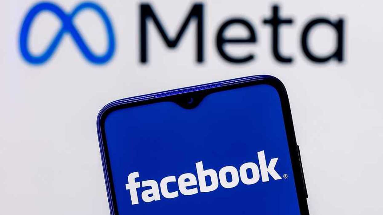 A cell phone held up with the word Facebook on it against a background that says Meta
