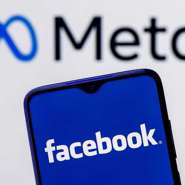 A cell phone held up with the word Facebook on it against a background that says Meta