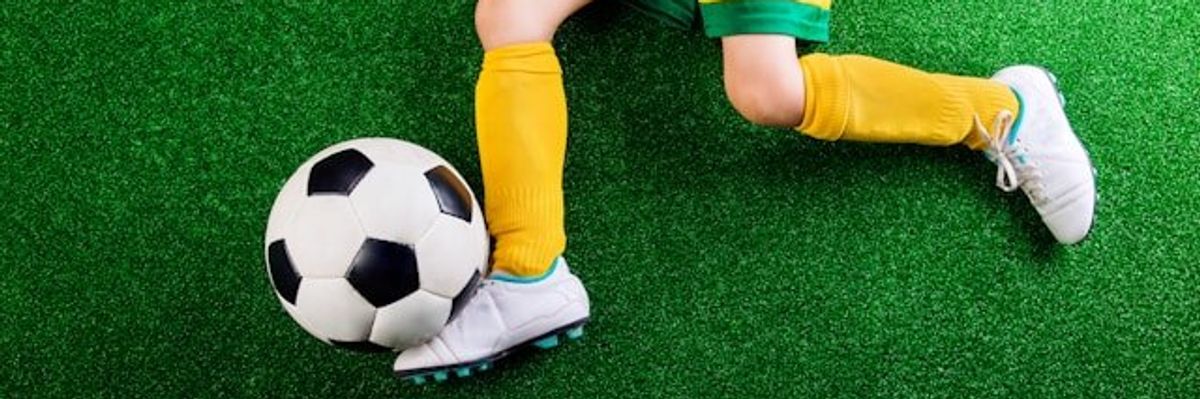 A child laying on an artificial turf surface with a soccer ball
