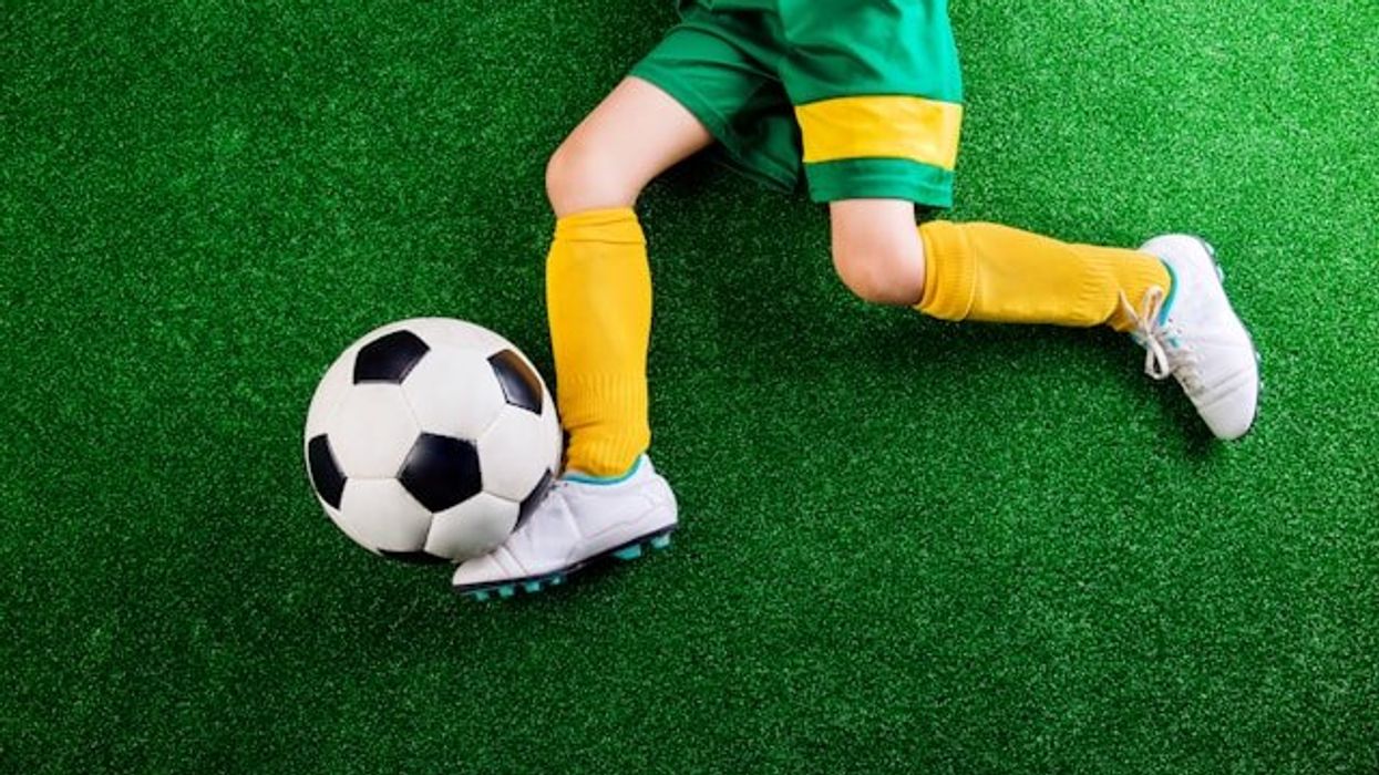 A child laying on an artificial turf surface with a soccer ball