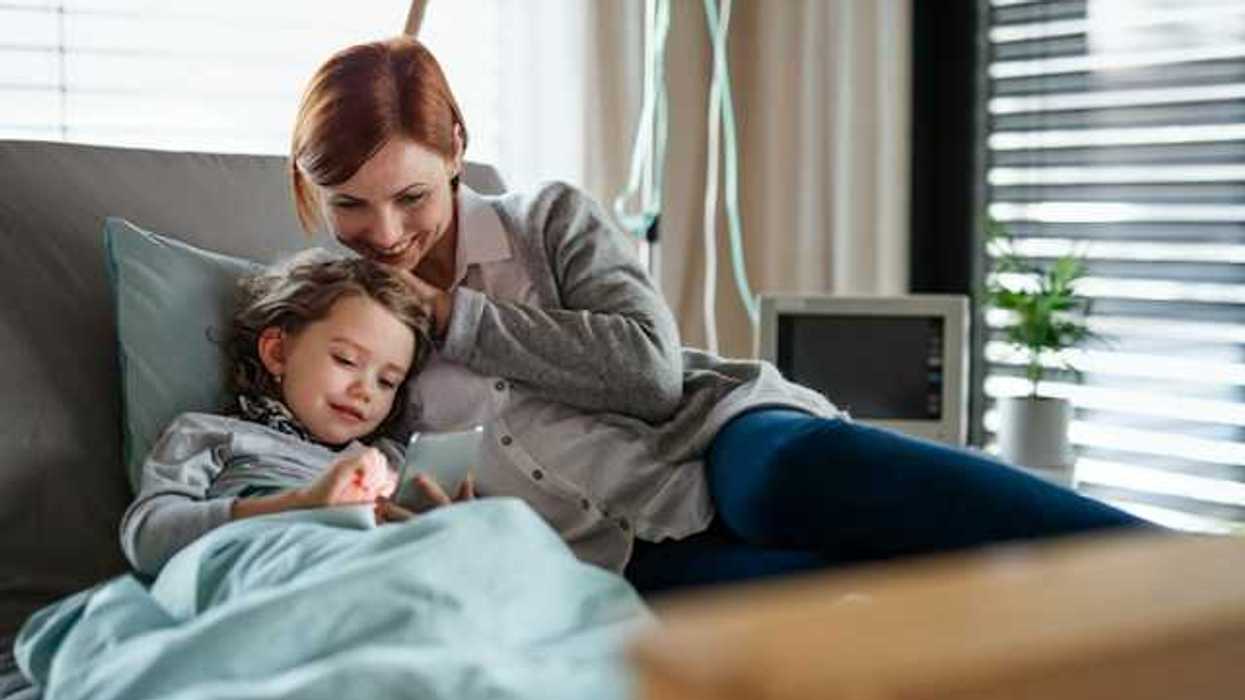 A child looking at a phone with her mother while in a hospital bed
