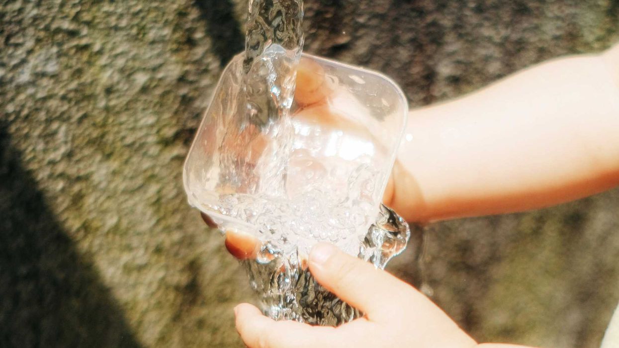a child's hands pouring water into a glass.