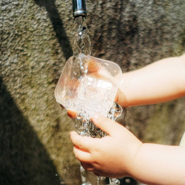 a child's hands pouring water into a glass.