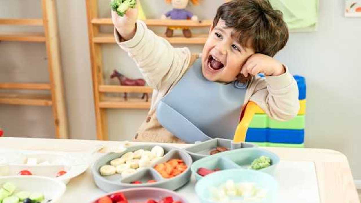 A child sitting at a table with a variety of fruits and vegetables on plates in front of him