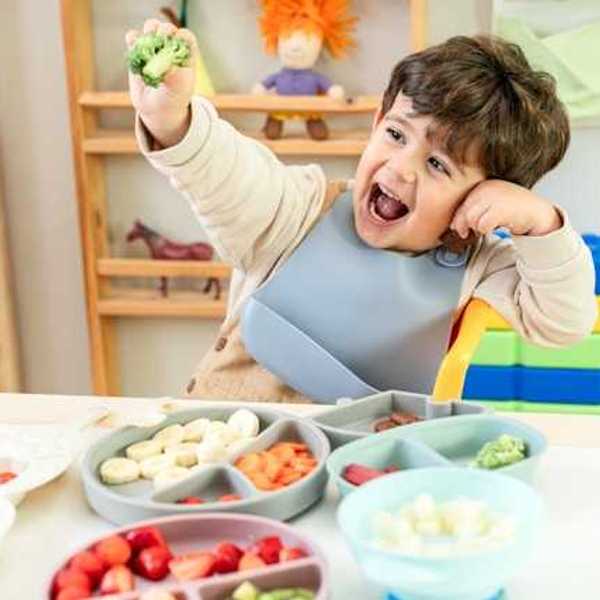 A child sitting at a table with a variety of fruits and vegetables on plates in front of him