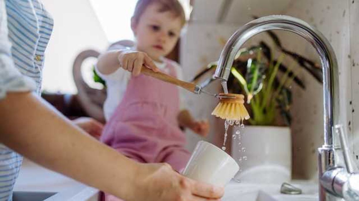 A child sitting on the counter helping mom wash a cup