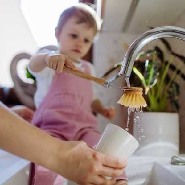 A child sitting on the counter helping mom wash a cup