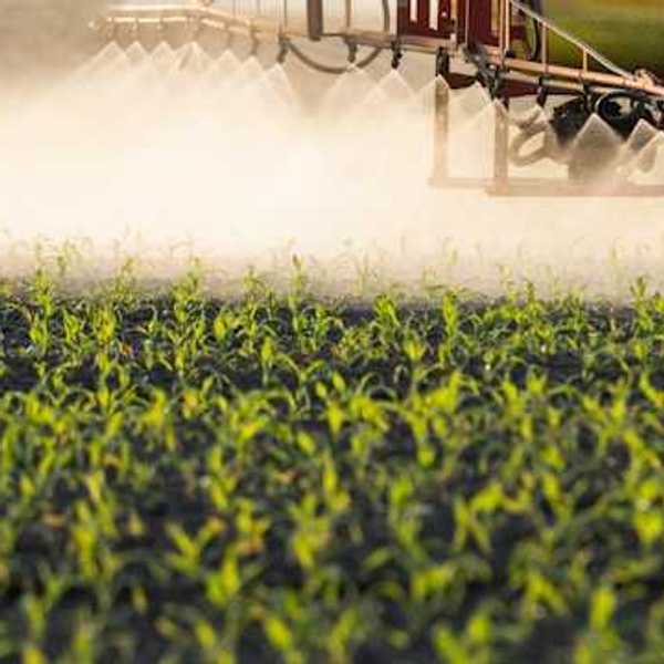 A closeup of a farm tractor applying pesticides to a green field