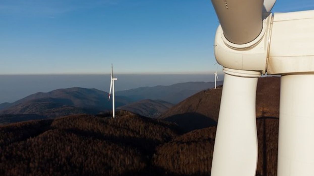 A closeup of a wind turbine situated on a mountain ridgeline.