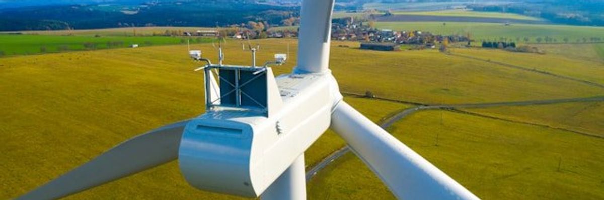 A closeup of a wind turbine with green fields in the background.