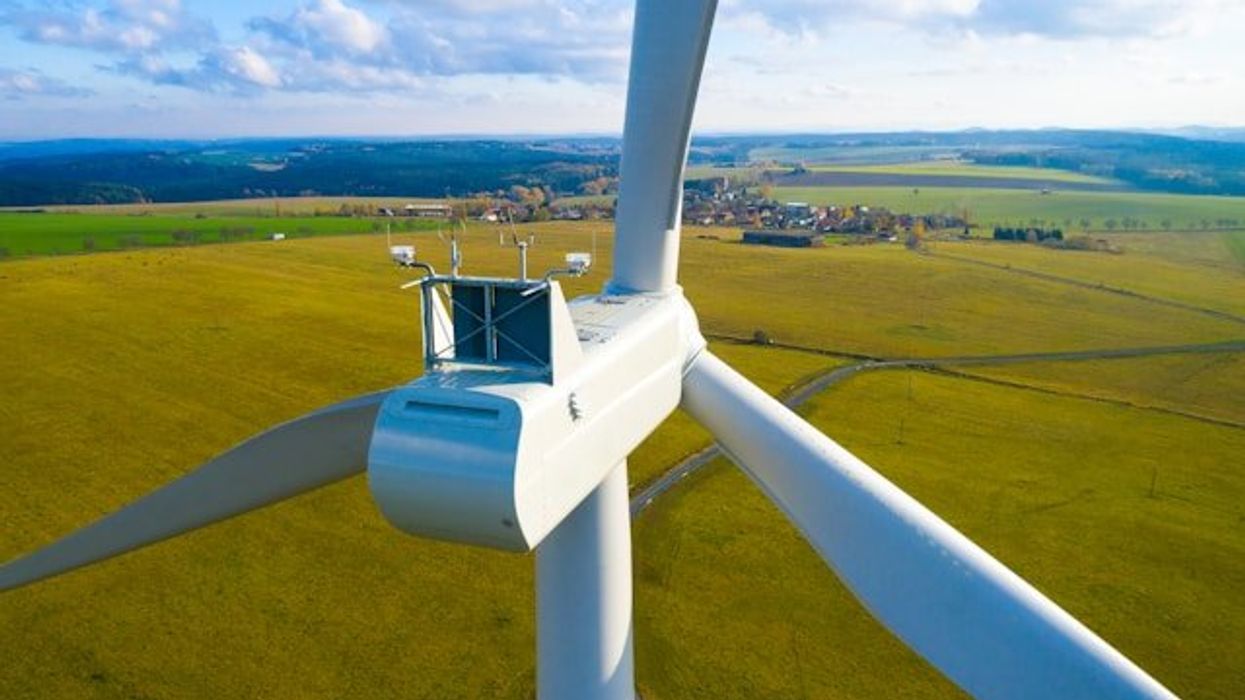A closeup of a wind turbine with green fields in the background.