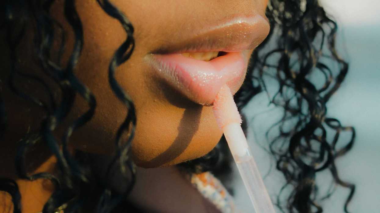 A closeup of a woman's nose and lips, applying lip gloss.