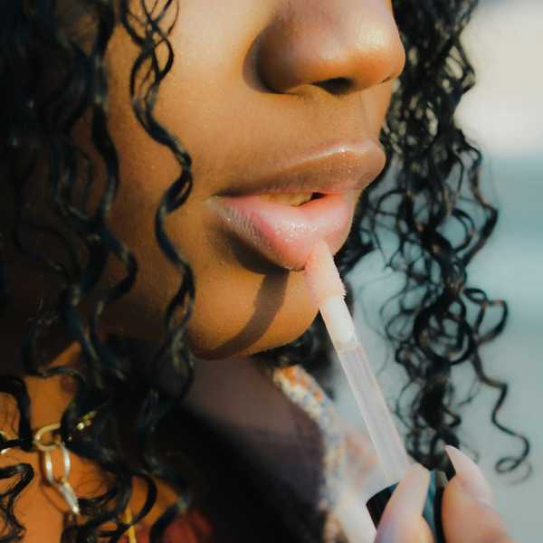 A closeup of a woman's nose and lips, applying lip gloss.
