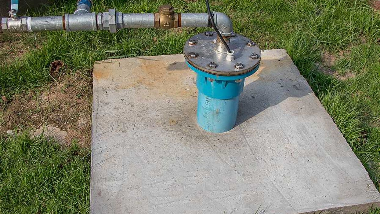 A concrete pad with a well pump and silver pipes coming out of it