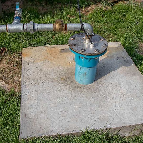 A concrete pad with a well pump and silver pipes coming out of it