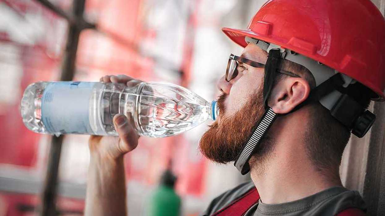 A construction worker in a red hard hat drinking from a plastic water bottle