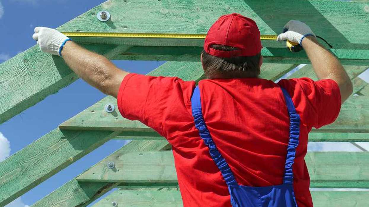A construction worker measuring wooden trusses