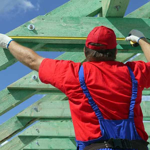 A construction worker measuring wooden trusses