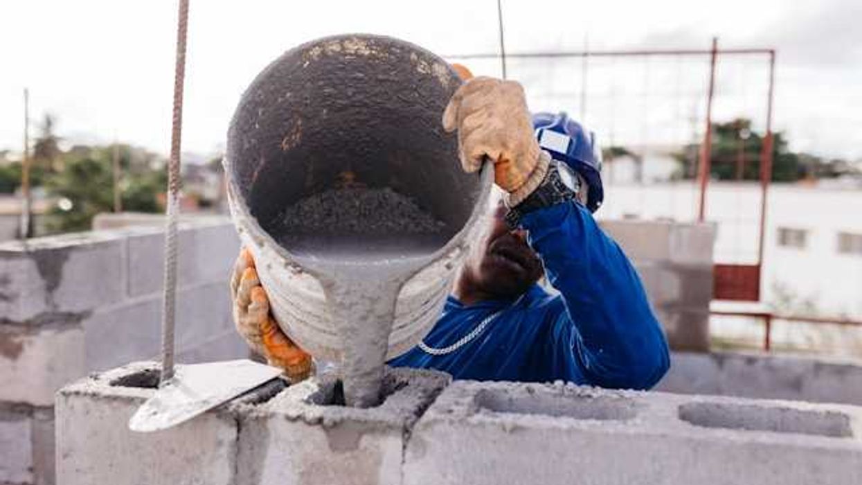 A construction worker pouring cement into open bricks