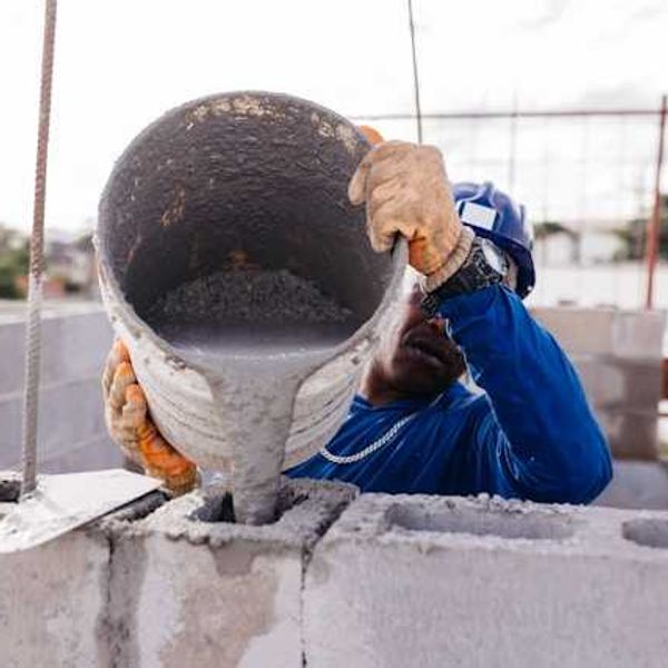 A construction worker pouring cement into open bricks