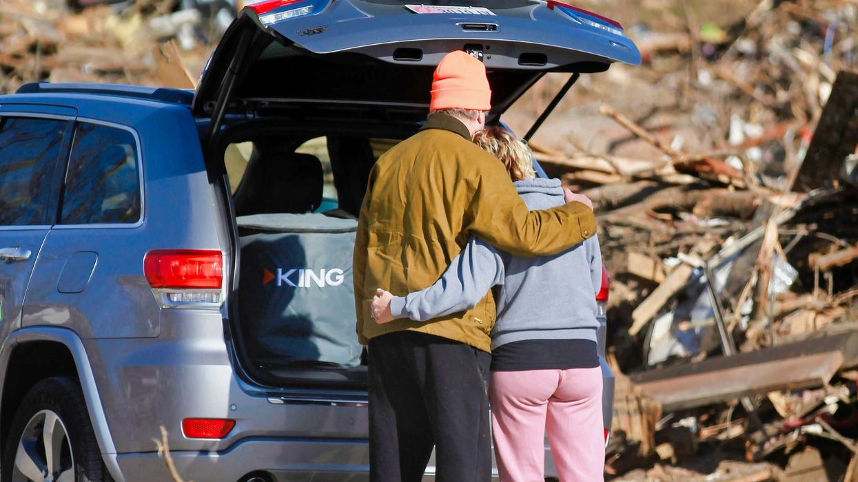 a couple of people standing next to a car in front of a destroyed home
