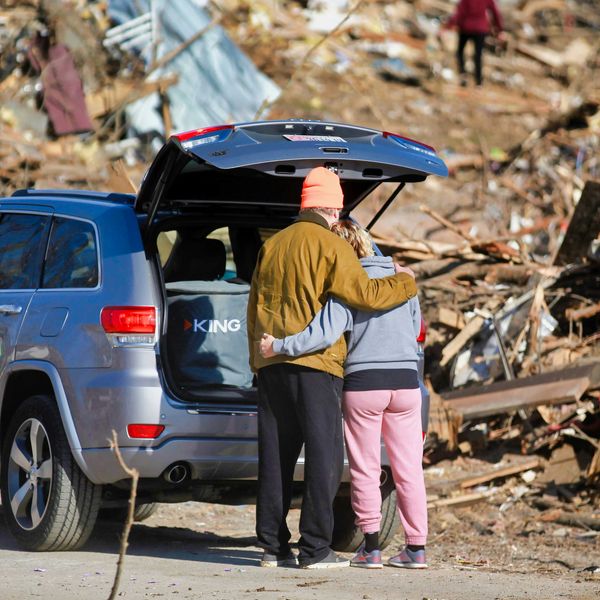 a couple of people standing next to a car in front of a destroyed home
