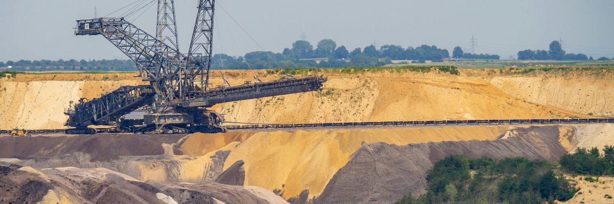 A crane in a mining pit with fields and trees in background.