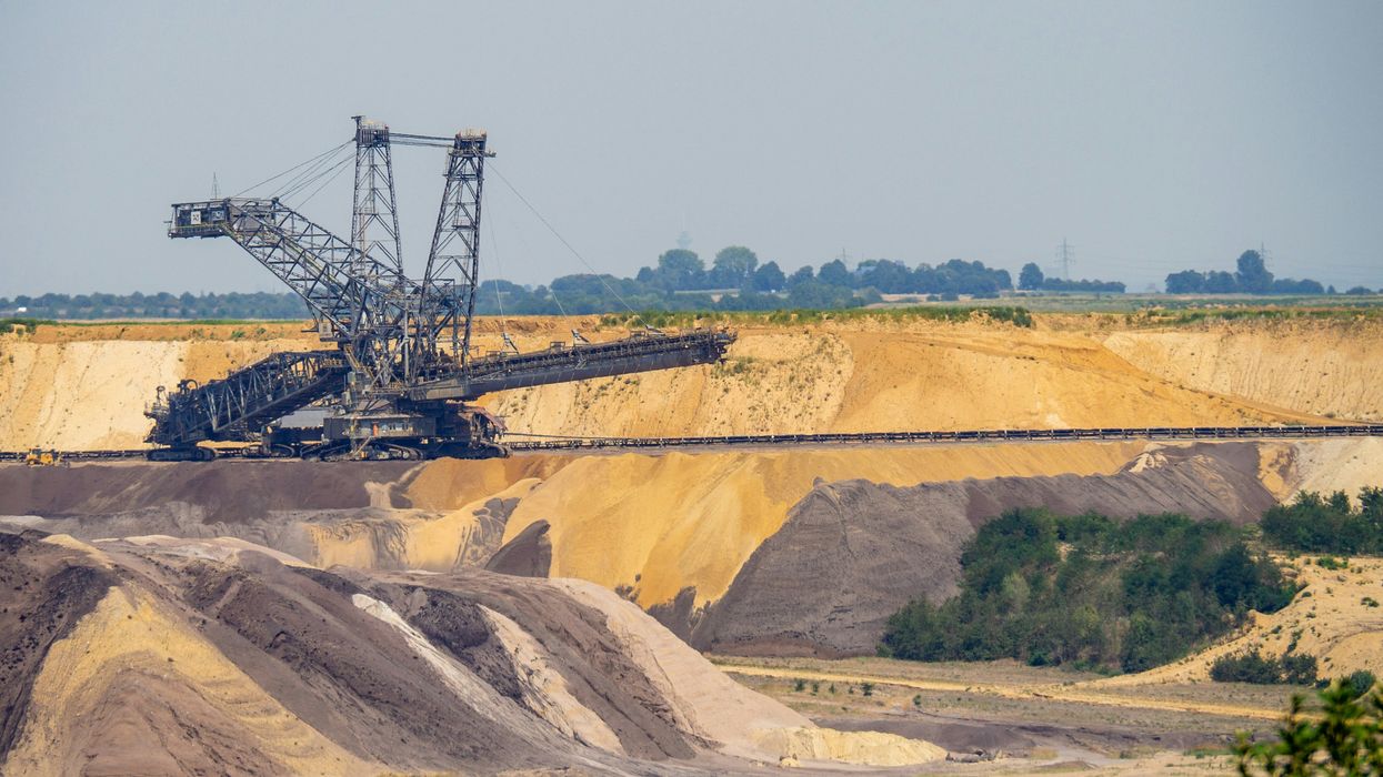 A crane in a mining pit with fields and trees in background.