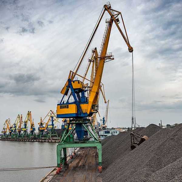 A crane lifting coal from a pile along a dock