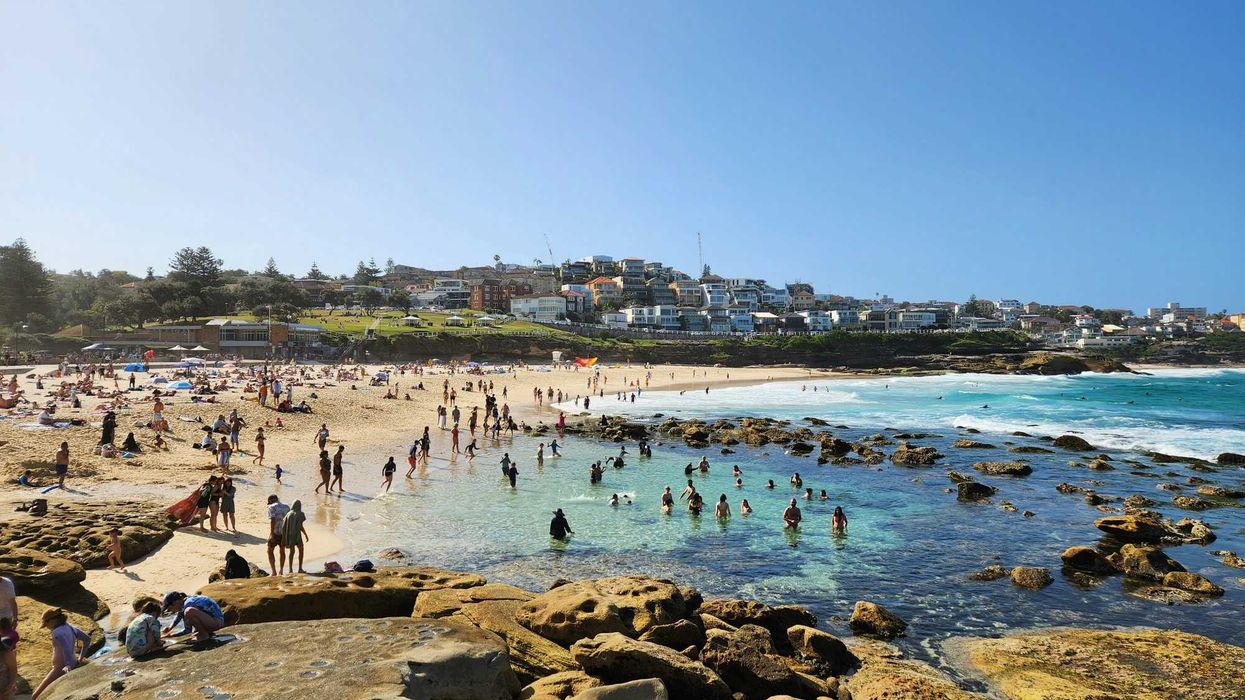a crowded beach with lots of people on it and buildings in background.