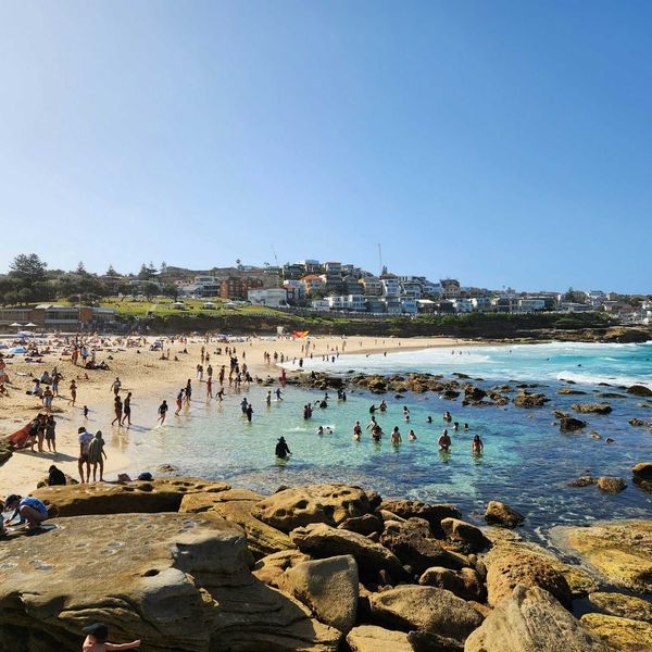 a crowded beach with lots of people on it and buildings in background.