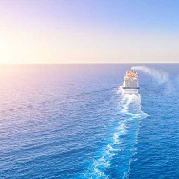 A cruise ship in the middle of the ocean with the sun setting to the left