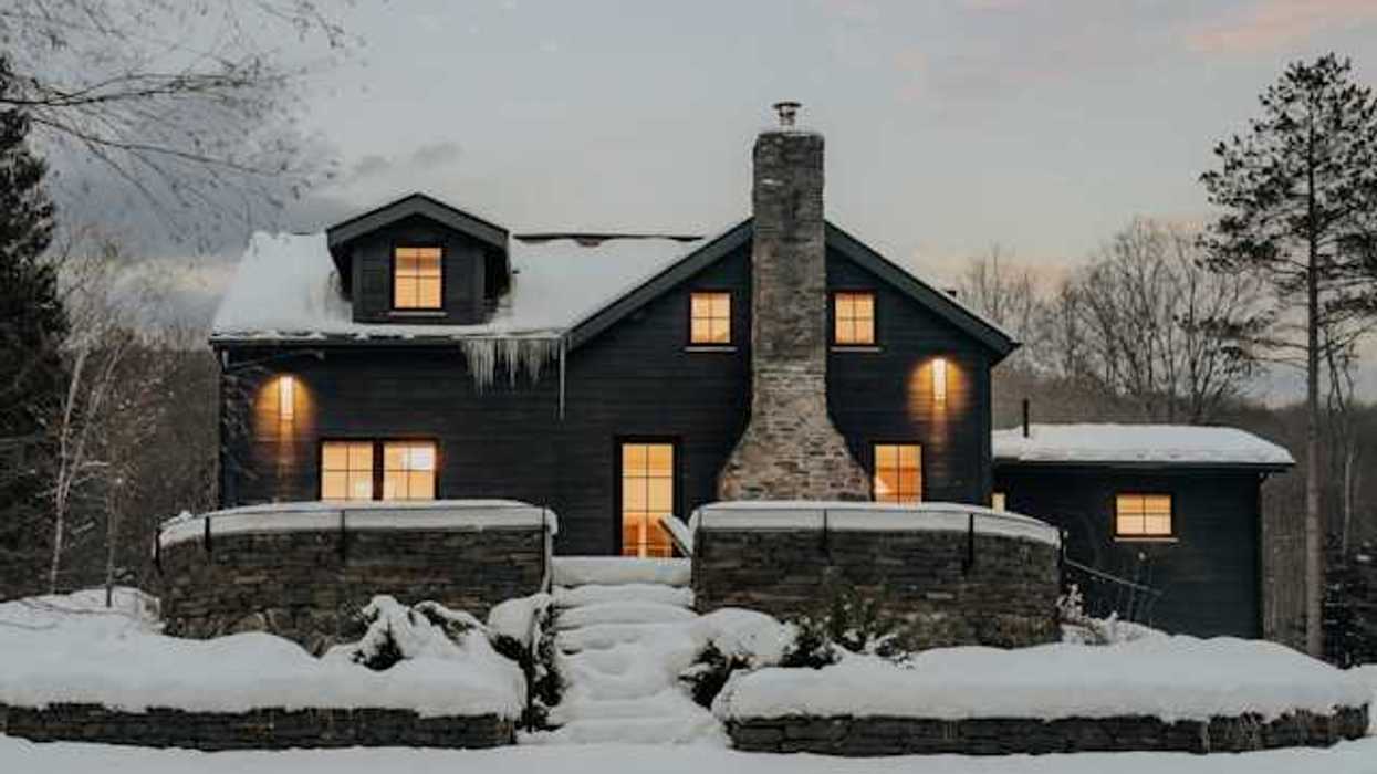 A dark house covered in snow with warm light coming from all of the windows