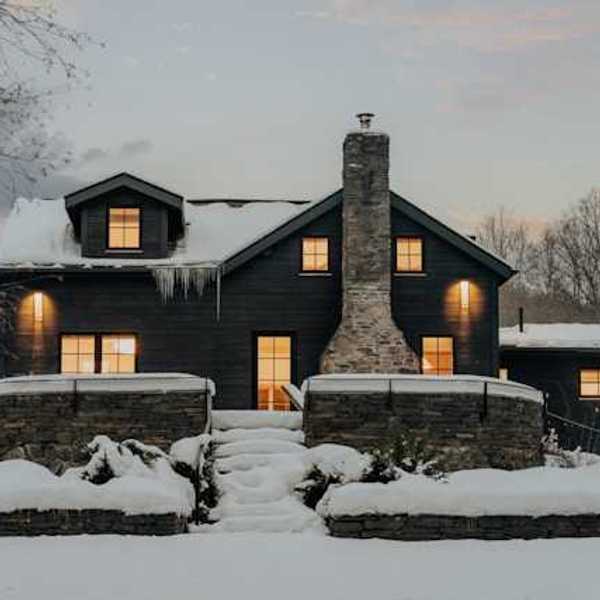A dark house covered in snow with warm light coming from all of the windows
