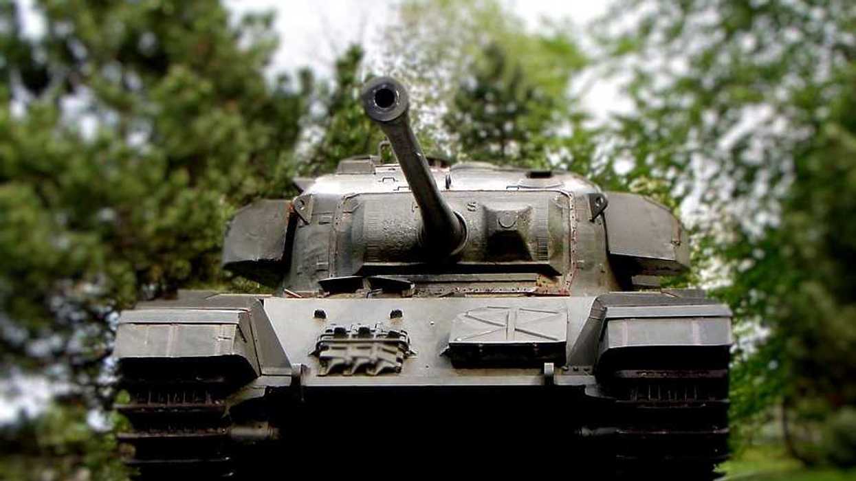 A dark military tank parked on green grass with trees in the background