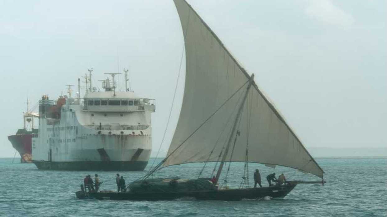 A dhow, a traditional sailing vessel for the region, sailing past a larger ship near the port of Zanzibar, Tanzania.