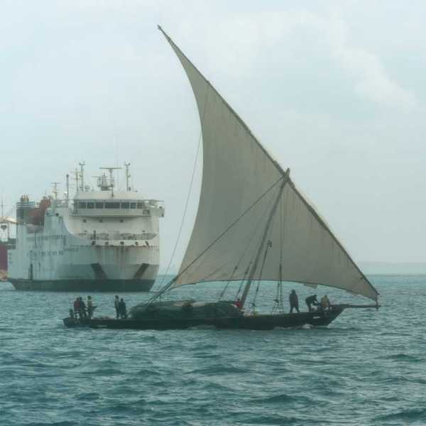 A dhow, a traditional sailing vessel for the region, sailing past a larger ship near the port of Zanzibar, Tanzania.