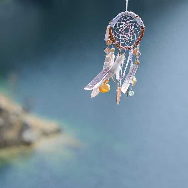 A dreamcatcher with feathers and twine with water in the background