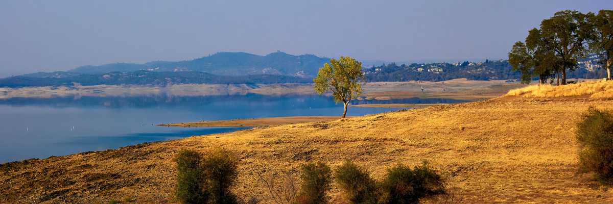 A dry field next to a reservoir with low water levels.
