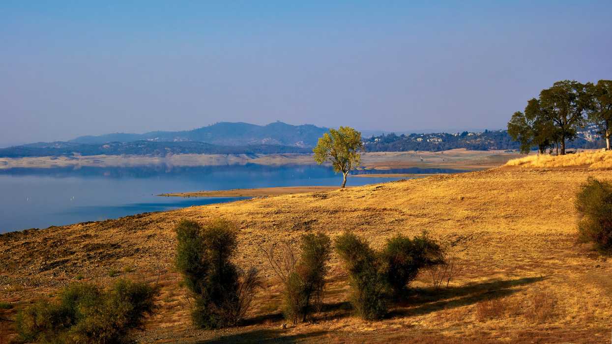 A dry field next to a reservoir with low water levels.