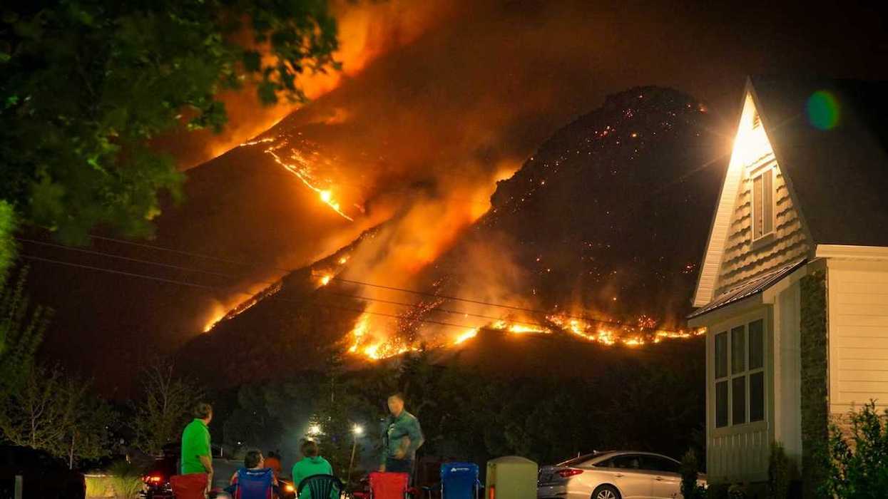 A family watches a nearby wildfire from their front lawn as flames cover a nearby mountainside in a nighttime setting
