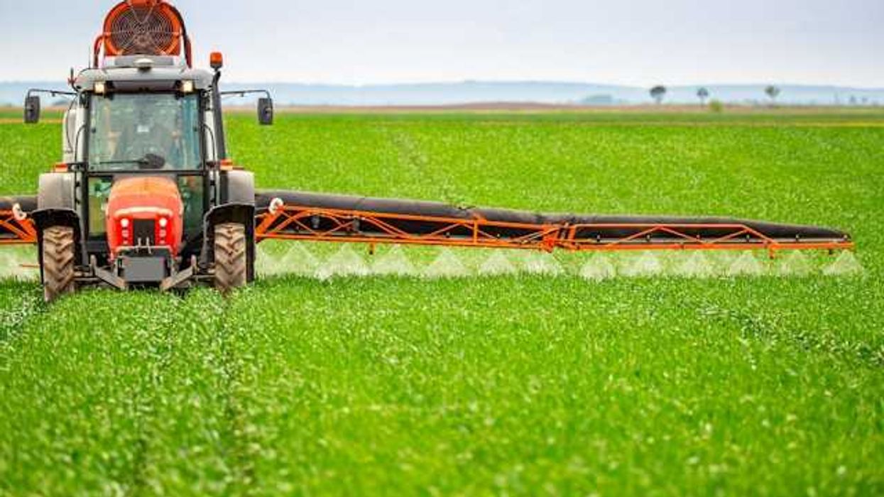 A farm tractor applying herbicide to a field