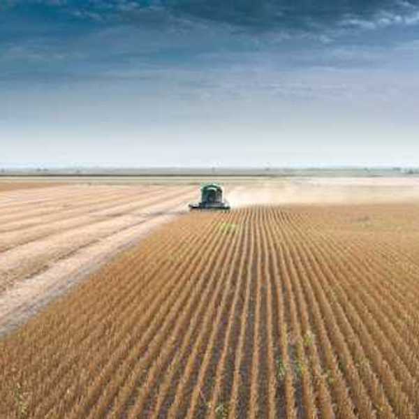 A farm tractor driving across a dry field
