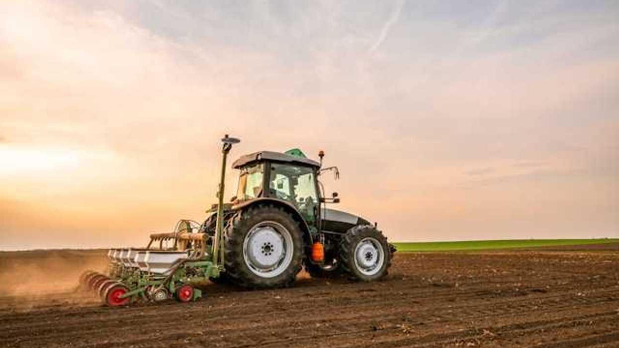 A farm tractor driving across a field of soil