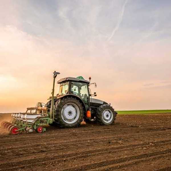 A farm tractor driving across a field of soil